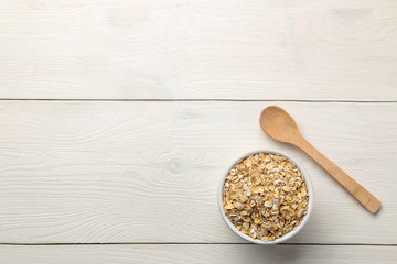 Dry oatmeal flakes in a bowl and spoon on a white wooden table. healthy nutrition. healthy food. top view