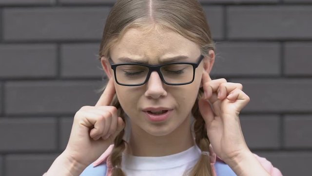 Scared teen girl covering ears from bullying, classmates calling names, teasing