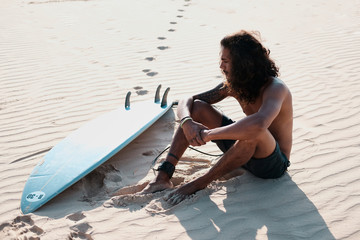 Man Surfer Sitting at Surfboard on Sand Beach