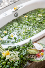Bathtub full of green leaves in water. Natural herbal bath. Spa-treat: Regenerating herbal bath with lime slices, lemongrass leaves and flowers. 