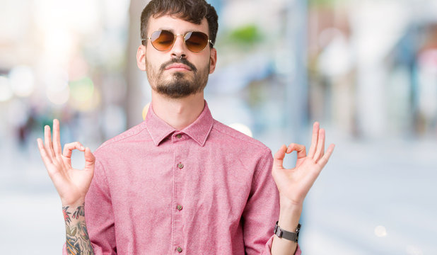 Young handsome man wearing sunglasses over isolated background relax and smiling with eyes closed doing meditation gesture with fingers. Yoga concept.