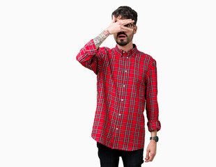 Young handsome man wearing glasses over isolated background peeking in shock covering face and eyes with hand, looking through fingers with embarrassed expression.