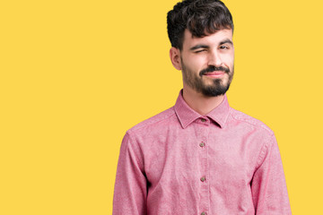 Young handsome man wearing pink shirt over isolated background winking looking at the camera with...