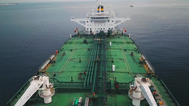 Green deck tanker ship underway in open water. Aerial, flying over. Ship's navigation bridge or superstructure showing radar electronics, lifeboat, no smoking and safety first signs on an oil tanker