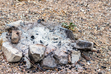 Graue Asche und Zigarettenkippe als Überreste von Lagerfeuer im Freien mit Steinen als Brandschutz zur Eindämmung der Brandgefahr und Feuergefahr der Feuerstelle beim Camping und Zelten