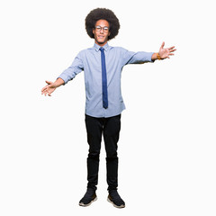 Young african american business man with afro hair wearing glasses looking at the camera smiling with open arms for hug. Cheerful expression embracing happiness.