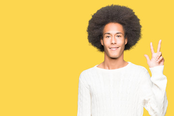 Fototapeta na wymiar Young african american man with afro hair wearing winter sweater showing and pointing up with fingers number three while smiling confident and happy.