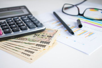 Calculating yen with 10,000 yen bank, calculator, Pen, paper and eyeglasses on white table