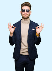Naklejka premium Young handsome elegant man wearing sunglasses relax and smiling with eyes closed doing meditation gesture with fingers. Yoga concept.