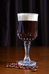 Irish coffee in a glass cup on a wooden table. Dark background.