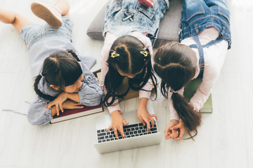 Three aisan children, Three sister, lay on the floor and use a laptop to do their...