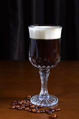 Irish coffee in a glass cup on a wooden table. Dark background.