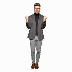 Young handsome business man wearing glasses celebrating surprised and amazed for success with arms raised and open eyes. Winner concept.