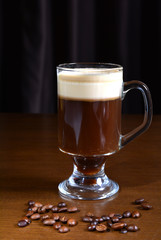 Irish coffee in a glass cup on a wooden table. Dark background.