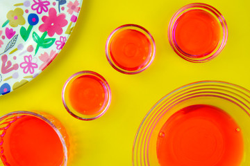 Red fruit juice in glass bowls and brightly colored plate on yellow background