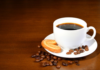 White cup of coffee and cookies on a saucer on a wooden table. Coffee beans. Dark background. Close-up.