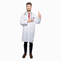 Young handsome doctor man wearing medical coat Swearing with hand on chest and fingers, making a...