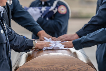 A group of military honor guard members place their gloves on the casket of a fallen hero in remembrance.