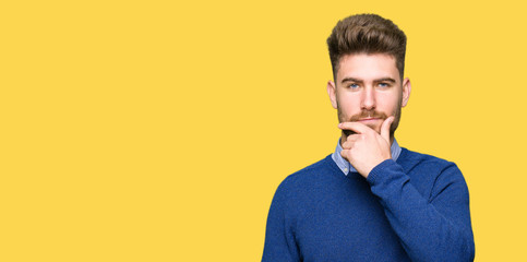 Fototapeta premium Young handsome bussines man looking confident at the camera with smile with crossed arms and hand raised on chin. Thinking positive.