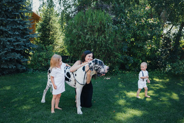 Obraz premium Family of brother and sister in white clothes play with a mom and a dog near them in the park or garden
