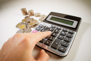 Man's hand is calculating many Thai coins with calculator. Close up.