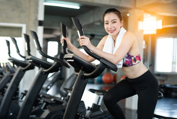 young asian woman exercising on bicycle in fitness center.beautiful Asian fitness girl on bicycle machine doing spinning at fitness. sport and Healthy concept. Workout with happiness ideas.