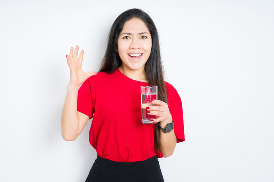 Young brunette woman drinking a glass of water over isolated background very happy and excited, winner expression celebrating victory screaming with big smile and raised hands