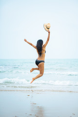 Beach summer holidays woman in happy freedom concept.Happy bikini woman jumping of joy on beach. Woman model wearing black bikini and beach hat on beach,Thailand.