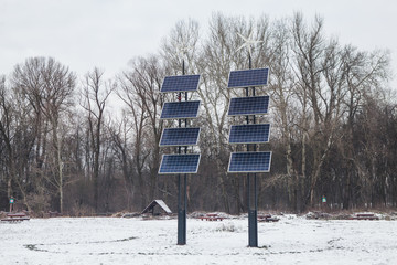 Solar stations in the park. Solar panels and wind turbines that generate electricity in a renewable green power plant against a cloudy sky in winter.
