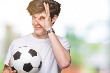 Young man holding soccer football ball over isolated background with happy face smiling doing ok...