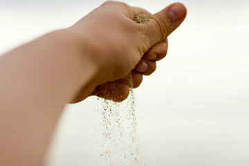 Hand releases a handful of falling sand. Summer beach vacation