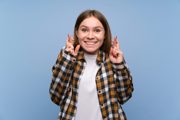 Young woman over blue wall with fingers crossing