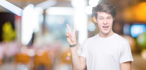 Young handsome man wearing casual white t-shirt over isolated background smiling with happy face winking at the camera doing victory sign. Number two.