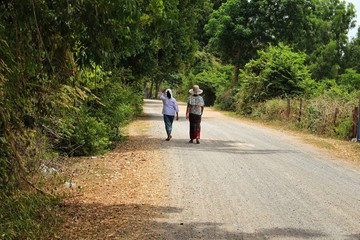 Local women wear sarong clothes on rural roads, surrounded by green nature