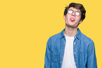 Young handsome man wearing glasses over isolated background sticking tongue out happy with funny expression. Emotion concept.