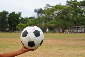 The boy holds the soccer ball beside the field