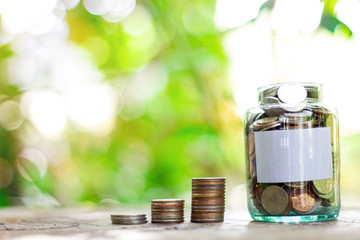 Saving money in a glass bottle. The background is green trees bokeh.