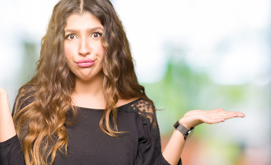 Beautiful young woman with long hair clueless and confused expression with arms and hands raised....