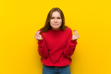 Young woman over yellow wall making money gesture