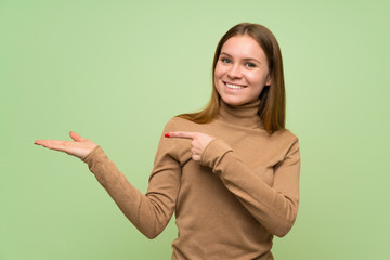 Young woman with turtleneck sweater holding copyspace imaginary on the palm to insert an ad