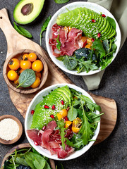 Low carbs bowl. Fresh salad with green spinach, rucola, avocado an ham serrano in white bowl, gray...
