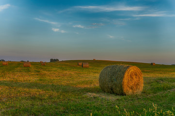 Large round hay bale on a farm field at sunset