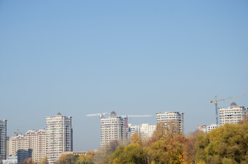 Obraz premium High-rise residential buildings and construction cranes on blue sky background. City in autumn