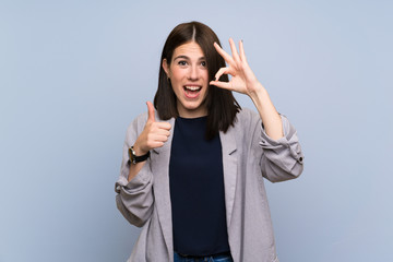 Young woman over isolated blue wall showing ok sign and thumb up gesture