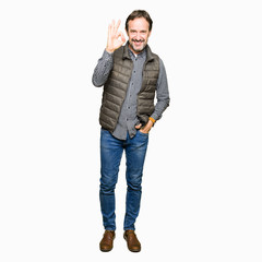 Middle age handsome man wearing winter vest smiling positive doing ok sign with hand and fingers....