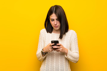 Young woman over isolated yellow wall sending a message with the mobile