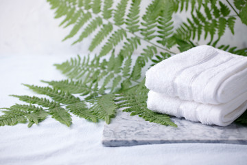 Beautiful composition of spa treatment with white cotton towels on marble plate and fern branches, minimal spa relax concept, eco friendly, natural cosmetic background