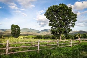 Fototapeta na wymiar Beautiful old wooden fence in amazing green mountain landscape with cloudy blue sky