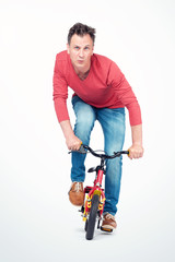 Funny man in jeans and a red T-shirt is rolling on a children's bike. Front view.
