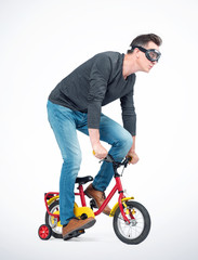 Fototapeta na wymiar Funny man in goggles, jeans and black t-shirt pedals a children's bicycle